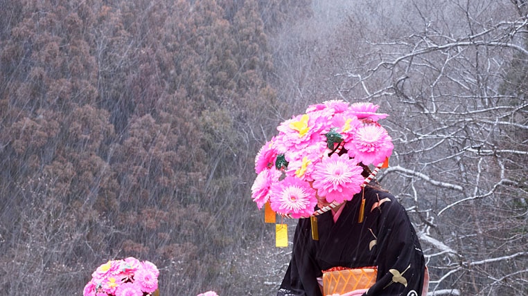Three Japanese woman with pink flower hats and Japanese gowns stand in the snow.