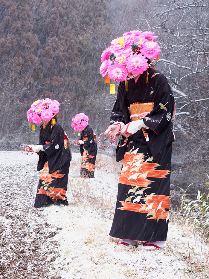 Three Japanese woman with pink flower hats and Japanese gowns stand in the snow.