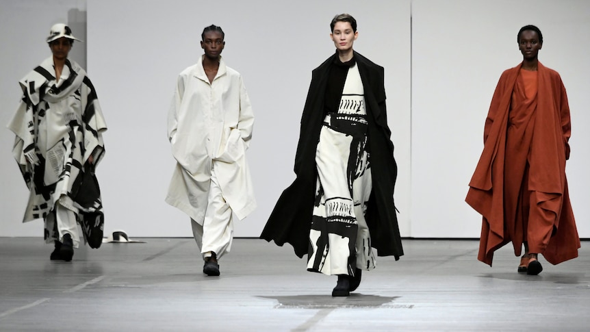 Four models in flowing clothes walk a runway.