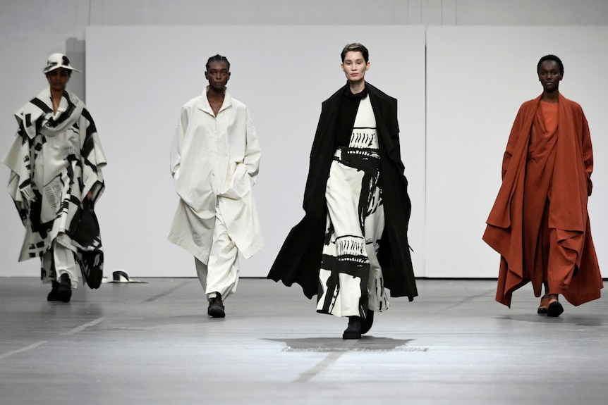 Four models in flowing clothes walk a runway 