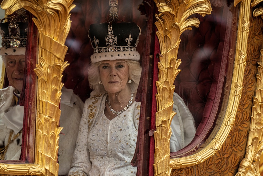 Camilla, wearing her crown, looks out the window of the Gold State coach