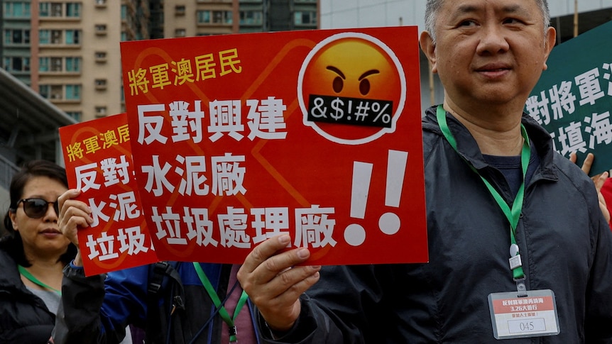 Asian people hold orange and white signs with Chinese writing in protest on city street
