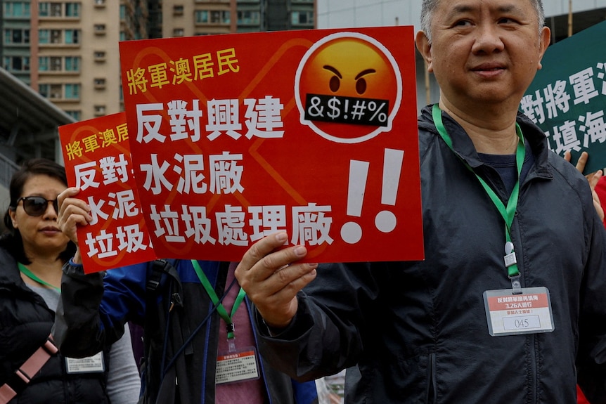 Asian people hold orange and white signs with Chinese writing in protest on city street