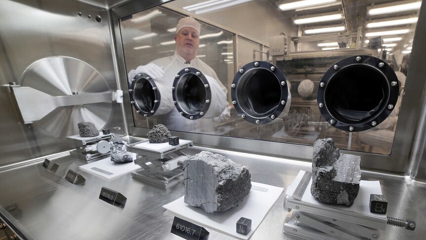 Apollo sample curator Ryan Zeigler stands next to a nitrogen-filled sealed case displaying various lunar rock samples.