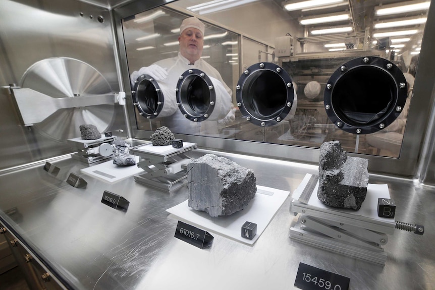 Apollo sample curator Ryan Zeigler stands next to a nitrogen-filled sealed case displaying various lunar rock samples.