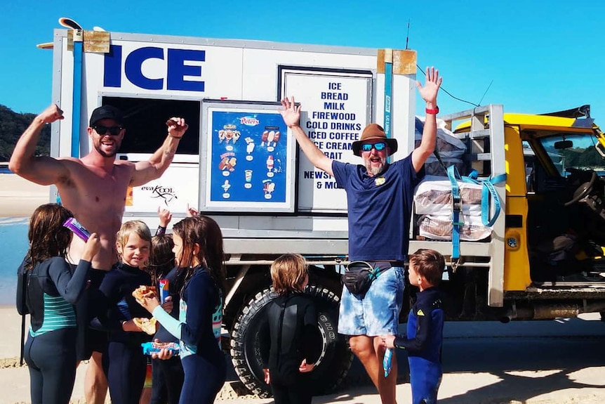 Two men standing in front of an ice truck.