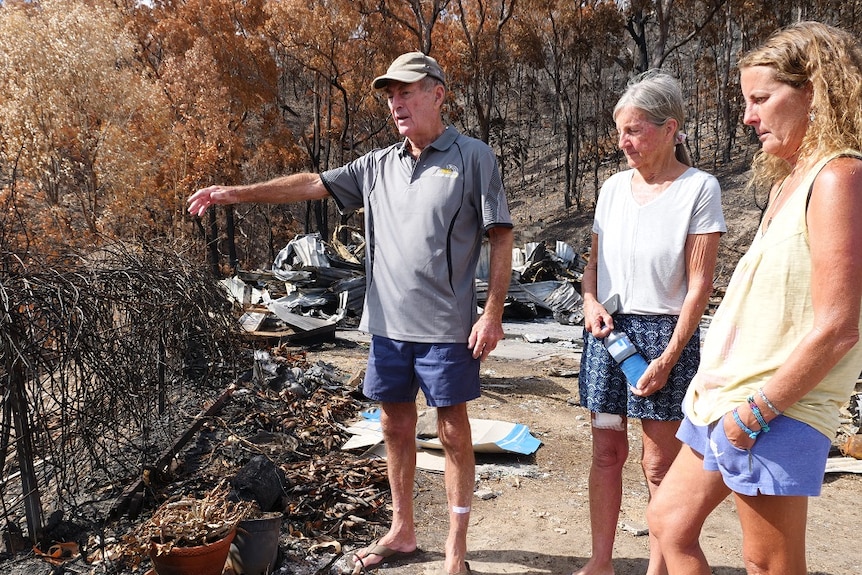 Greg points at the blackened ground, while Petria Stack and daughter Shelley Scott watch on.