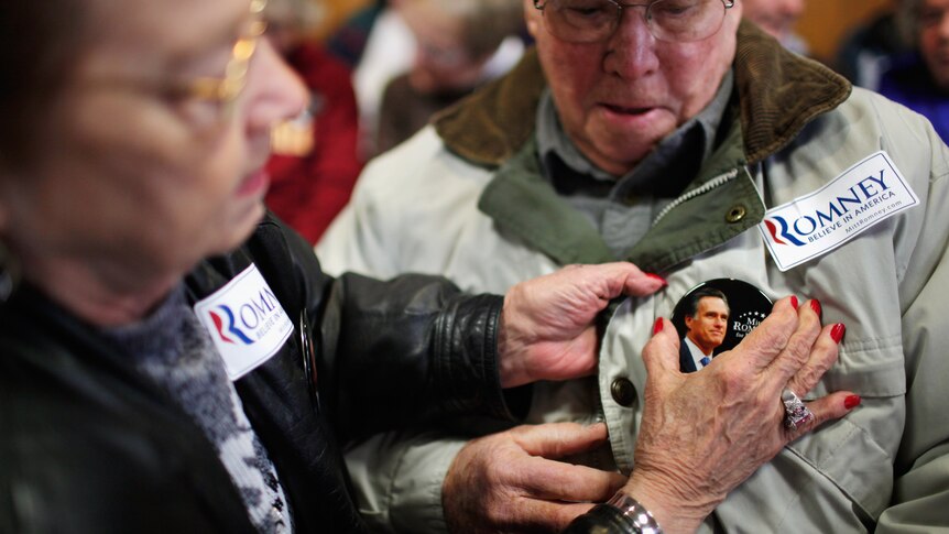Carol Barry helps pin a button on the jacket of friend Robert Wilson before a campaign rally with Mitt Romney