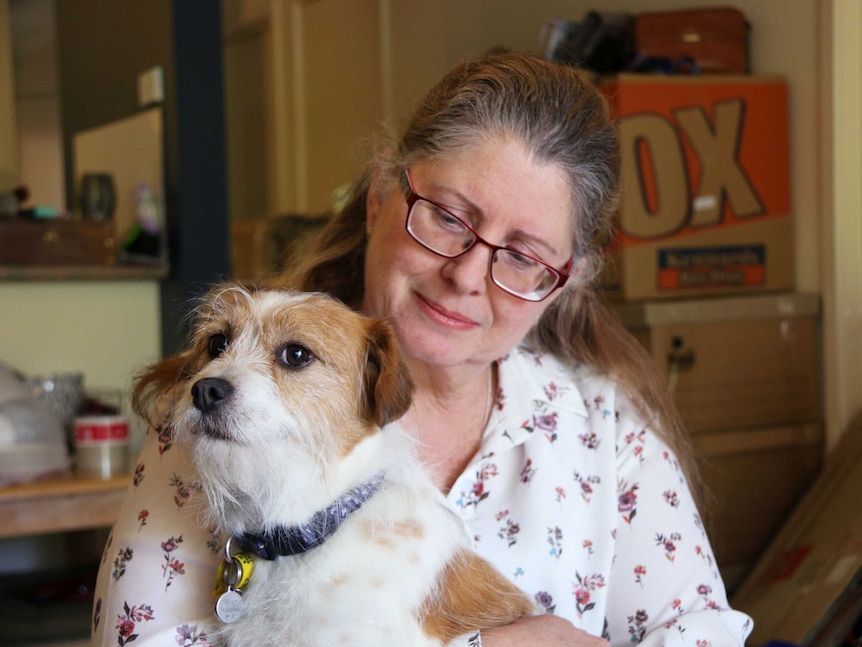 A woman smiles at her dog sitting on her lap.