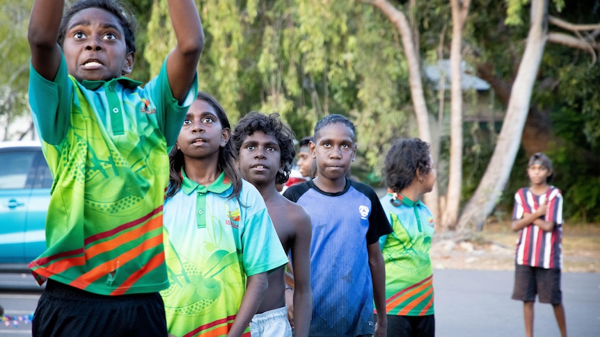 A young group of Indigenous kids, one of whom is about to shoot a basketball towards a hoop