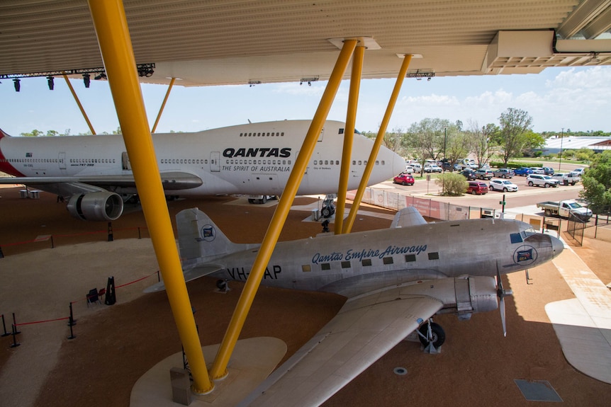 A Boeing 747 and an older, smaller airplane sit in an outdoor display under an enormous roof.