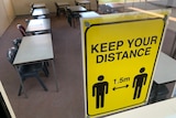 A yellow sign reading 'Keep Your Distance' on the window of an empty classroom