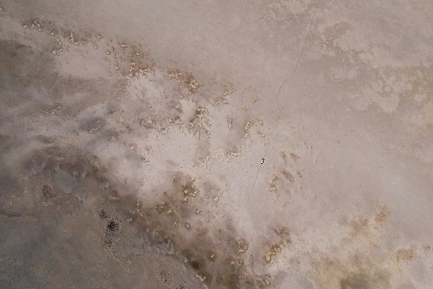 An aerial shot of a car driving across an open dirt landscape.