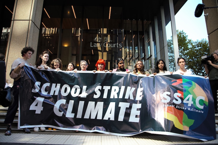 Nine teenagers and a guardian hold up a large sign saying "School Strike 4 Climate" outside the Federal Court.
