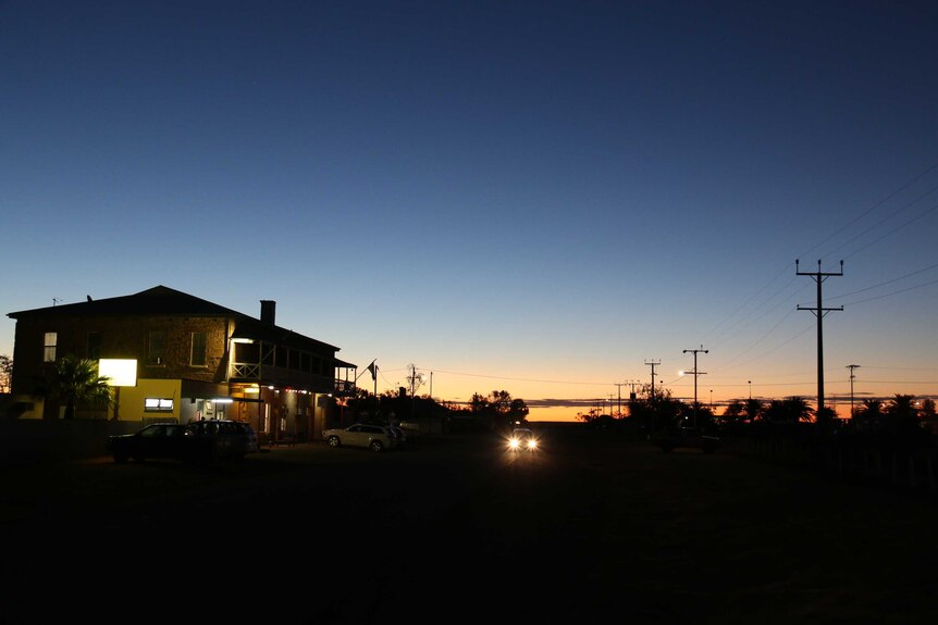 Landscape shot looking down a road with a pub in the foreground and sunset over the outback behind.