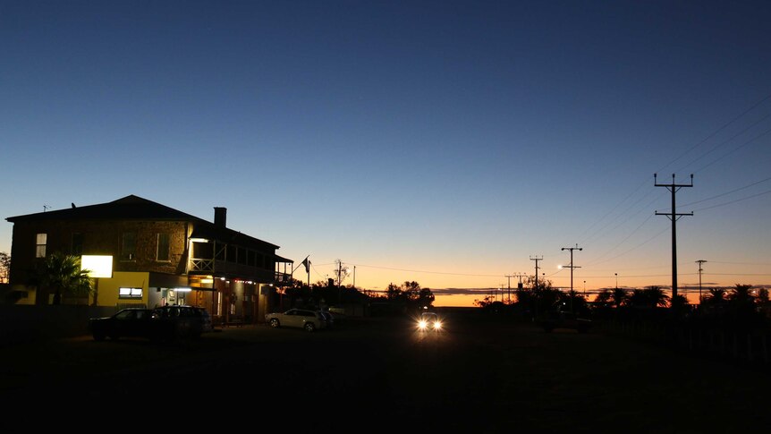 Landscape shot looking down a road with a pub in the foreground and sunset over the outback behind.