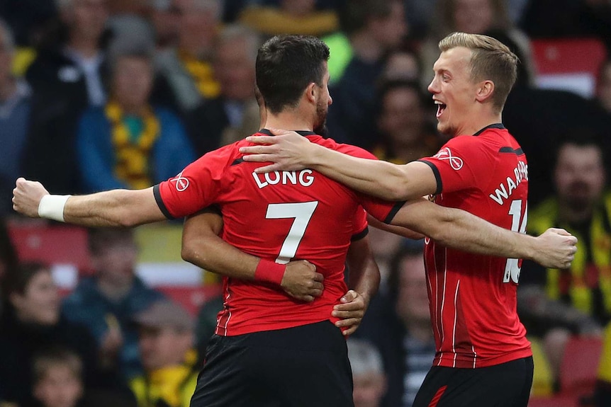 Shane Long wearing the number seven shirt with his back to the camera, holds his hands out wide as he is hugged by two teammates