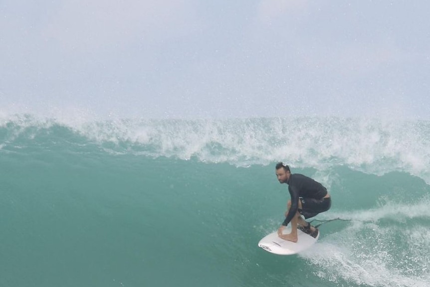 A man stand on his surfboard on a wave.