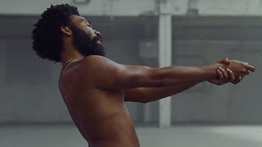 A screencap of Childish Gambino posing like he's holding a firearm from the 2018 'This Is America' music video