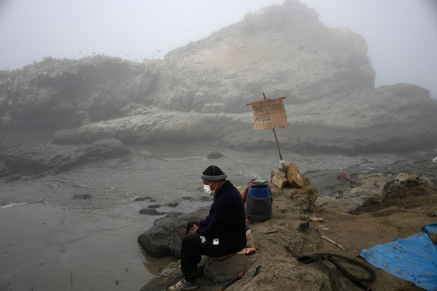 A man sits on the shore on a cloudy day. 