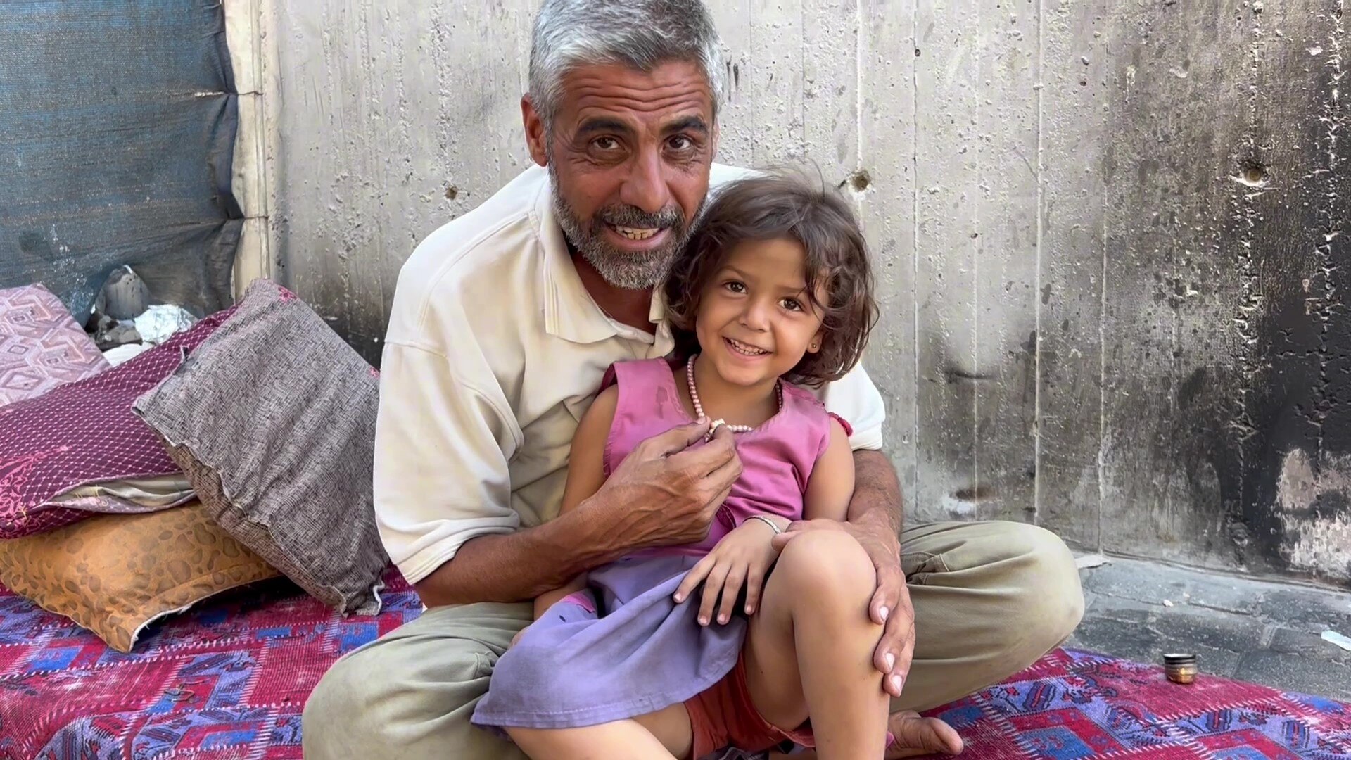 A man holds a young girl sitting on colourful mat.