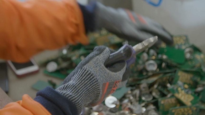 Gloved hand holds pliers and picks up waste computer circuit boards