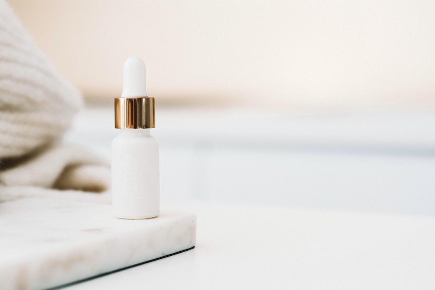 A white skincare bottle sits in a bathroom.