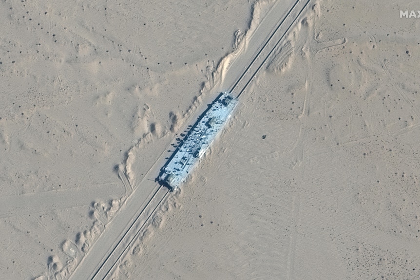 a satellite image taken from the air of a long vessel on rails. it's blue and surrounded by sand in the desert