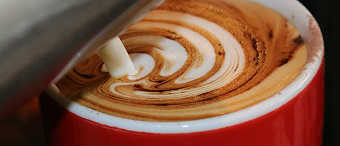 A barista pours milk into a cup of coffee