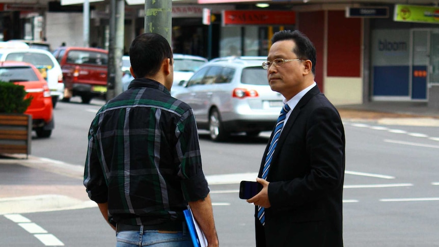 Eddie Kang stands on a street talking to a man.