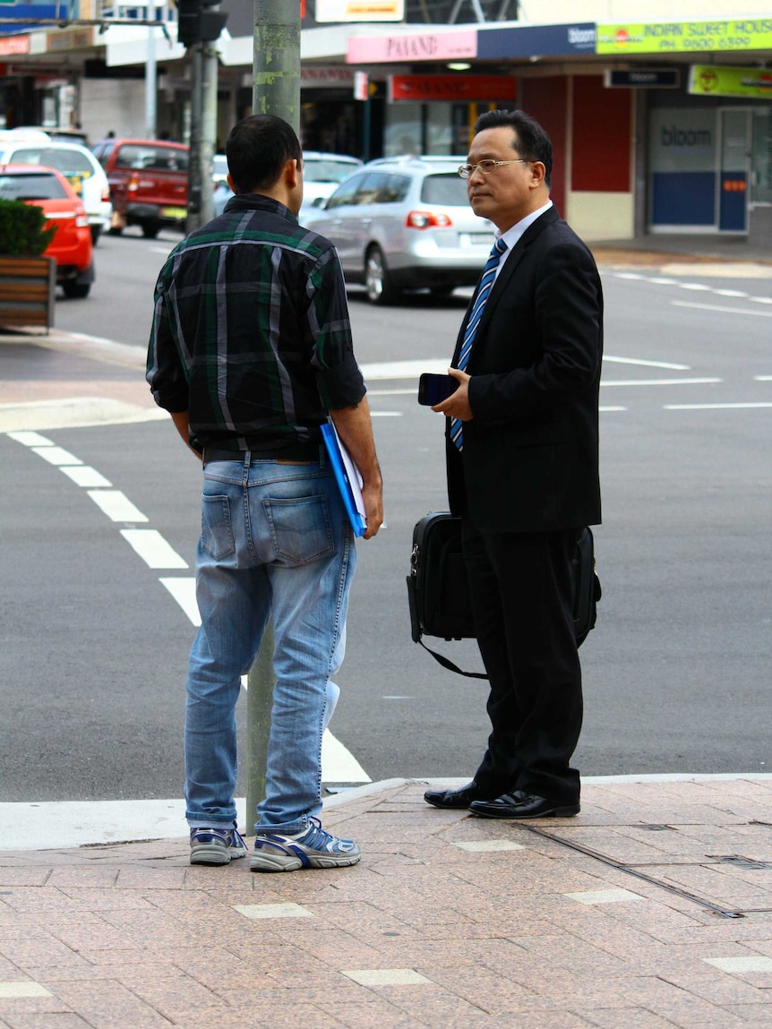 Eddie Kang stands on a street talking to a man.