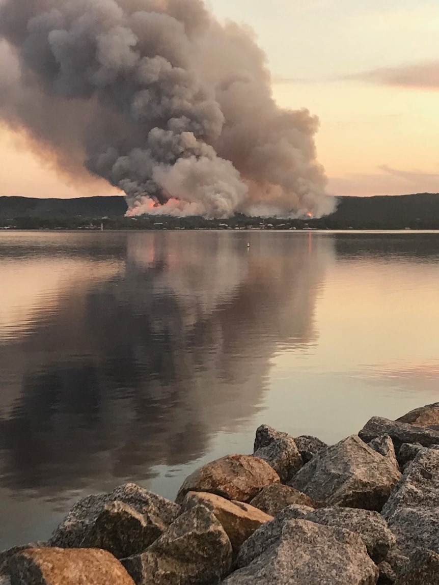 A bushfire viewed from across the water with a plume of smoke rising high into the air.