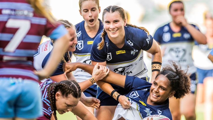 Female rugby players smile mid-tackle