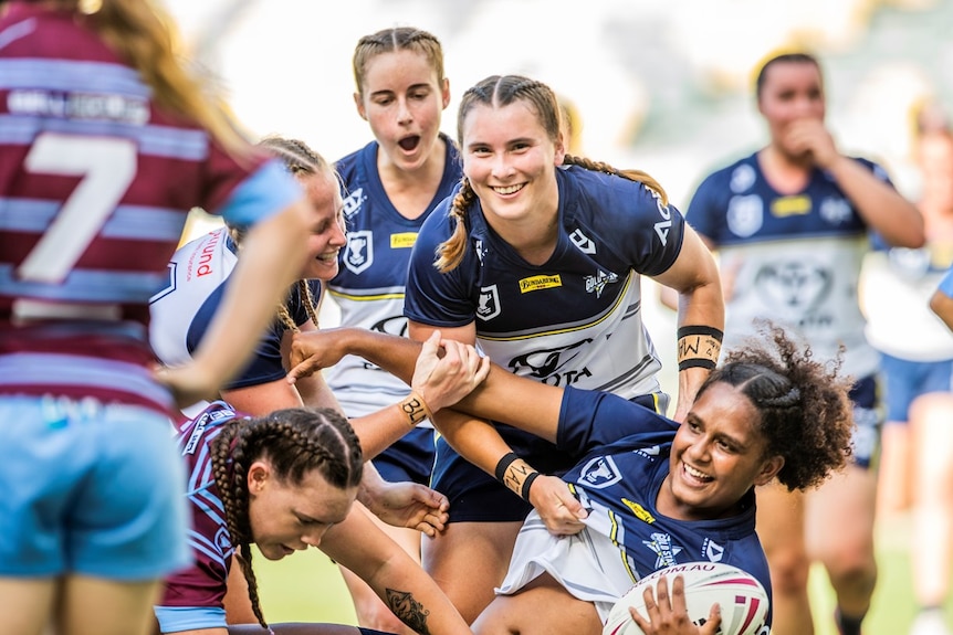 Female rugby players smile mid-tackle