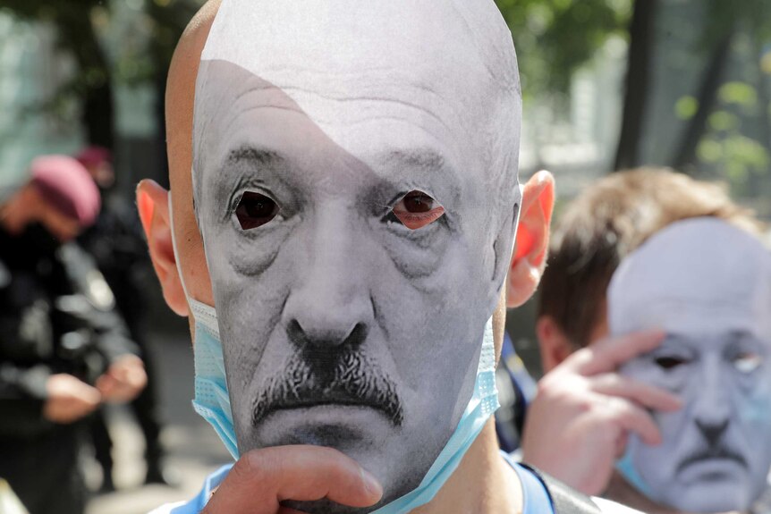 Two protesters hold paper masks of embattled Belarus President Alexander Lukashenko over their faces