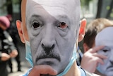 Two protesters hold paper masks of embattled Belarus President Alexander Lukashenko over their faces