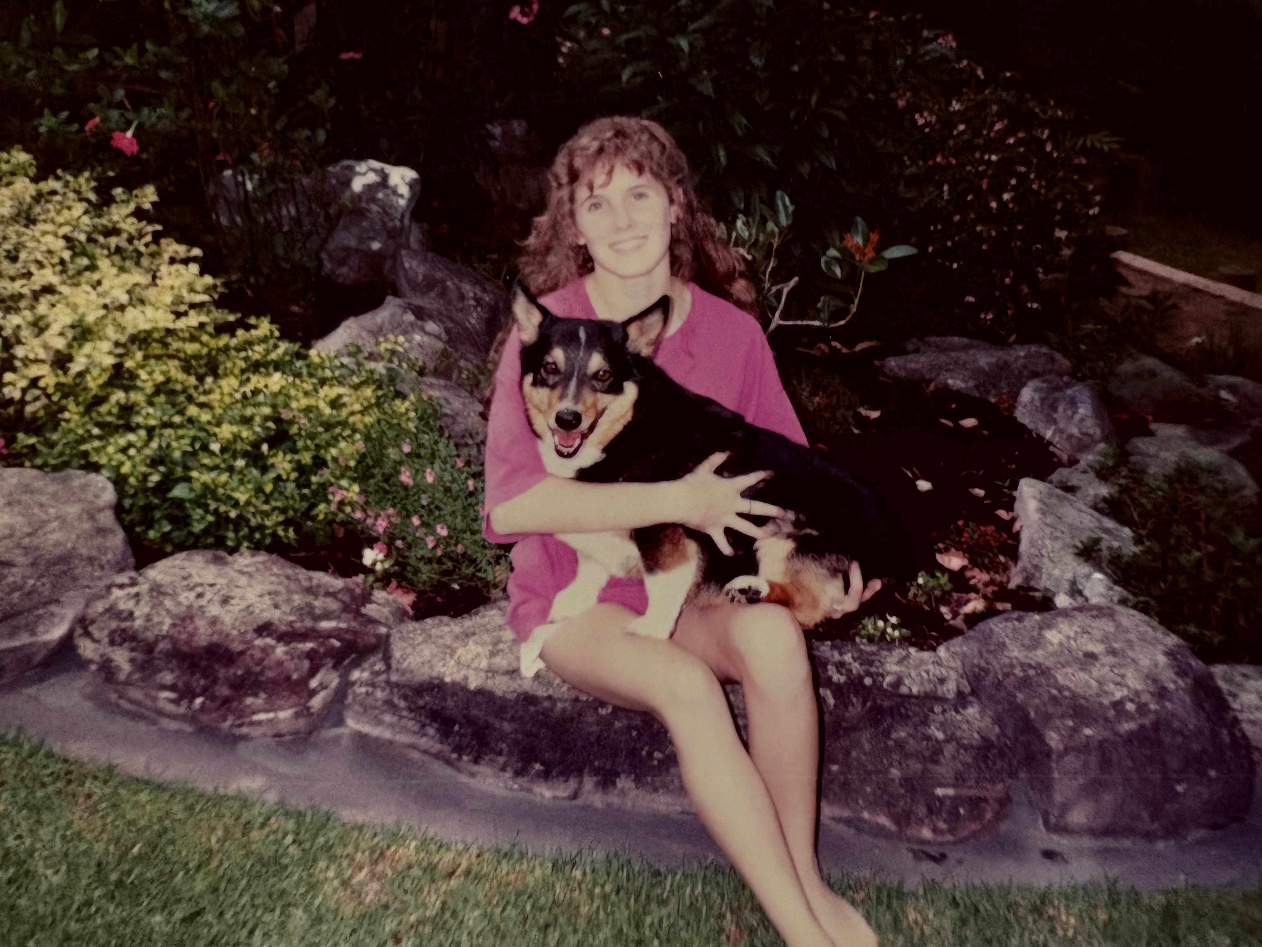 A girl sitting on a rock holding a dog on her lap