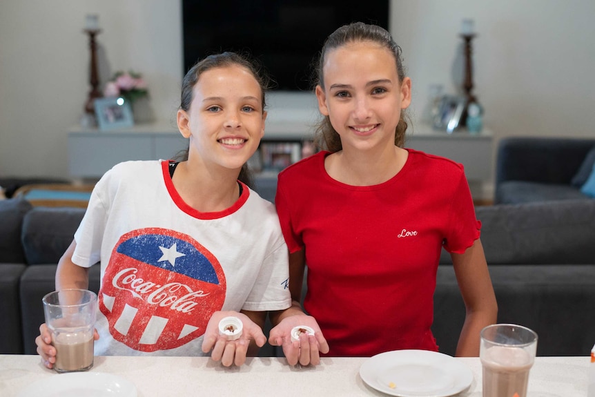 Sisters Ruby and Isobel Donaldson smile while holding a number of pills in their hand.