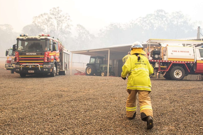 A female firefighter runs towards a truck as there is smoke and fire in the distance