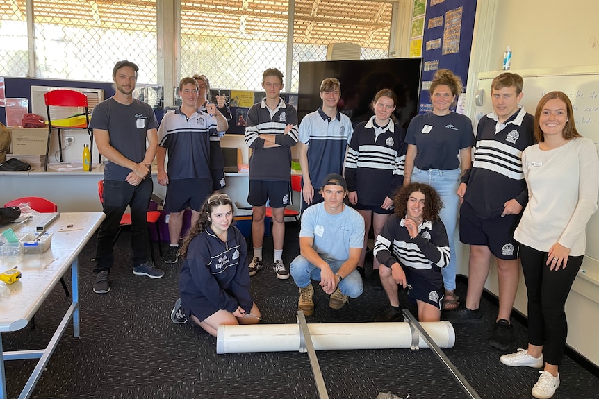 A group of students, their teacher stand behind a PVC pipe flotation rig.