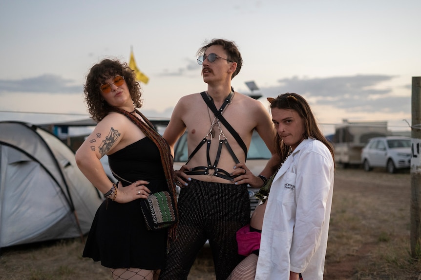 three people pose in costumes in front of a camp ground