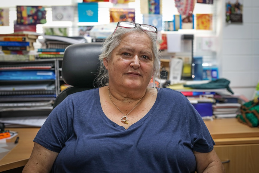 Dr.  Christine Jeffries-Stokes looks at the camera while sitting in her office with a stack of colorful books behind her