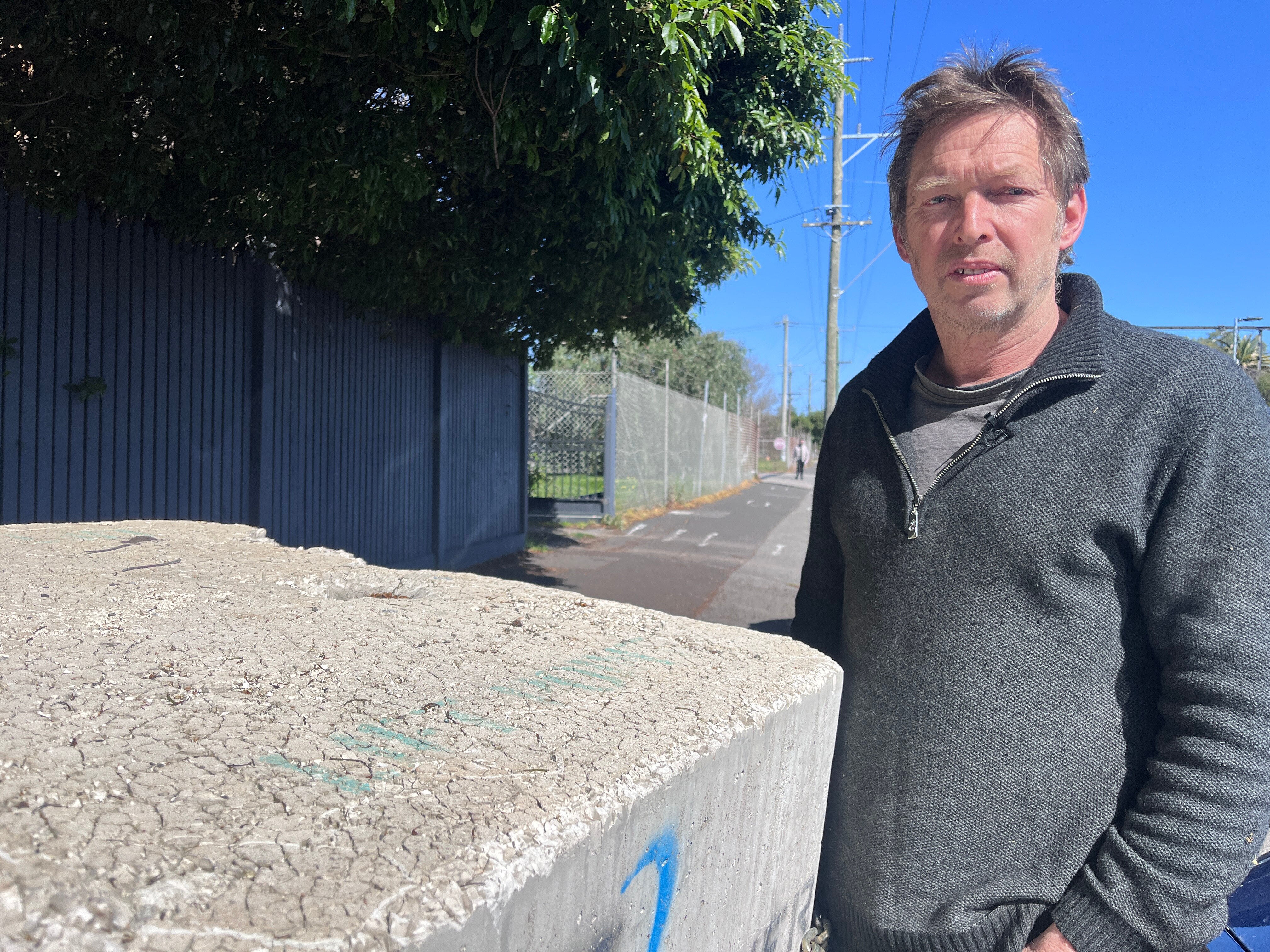 A man in a grey sweater standing next to a large concrete block. 