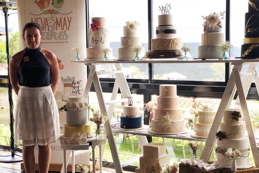 A woman stands next two a display of several elaborate wedding cakes