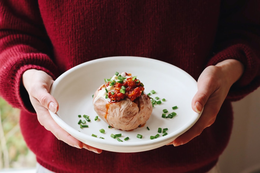 A baked potato on a plate, topped with a tomato mixture, sour cream, chives, a simple, vegetarian dinner for the family.