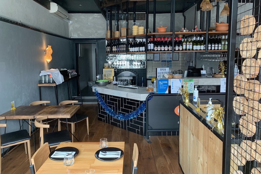 Empty chairs and tables inside a restaurant, where the bar is decorated with blue tinsel.