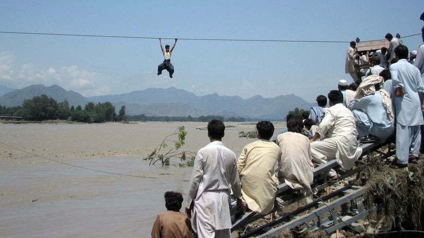 Onlookers perched on a damaged bridge watch a Pakistani flood survivor climb a rope