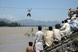 Onlookers perched on a damaged bridge watch a Pakistani flood survivor climb a rope