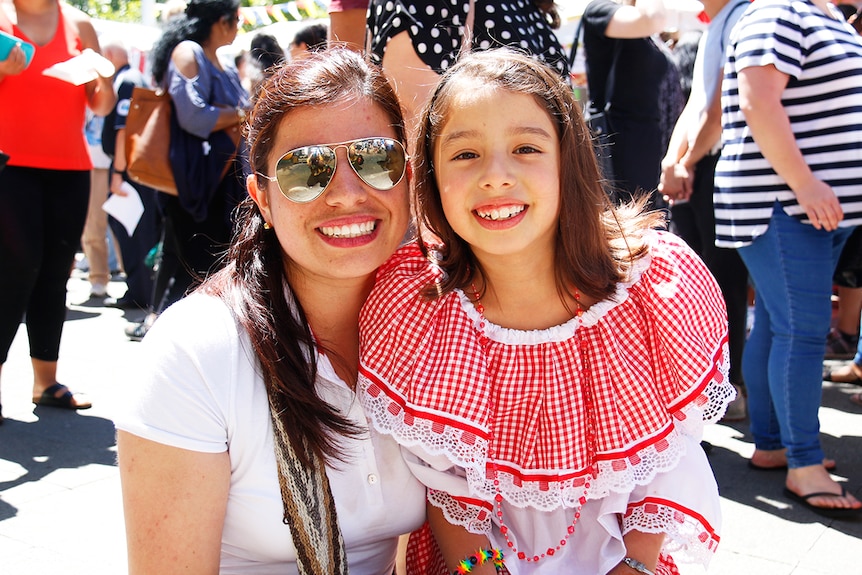 A woman hugs a little girl in a frilly, white and red dress.
