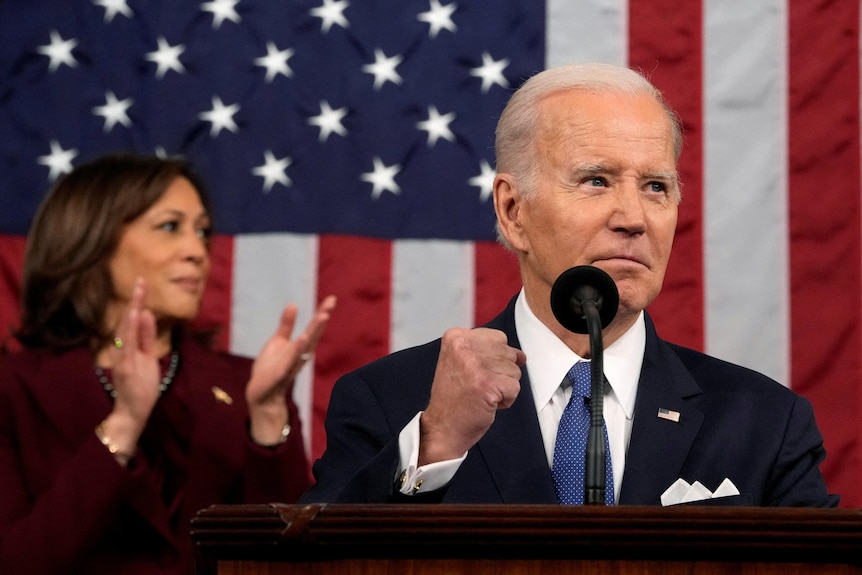 Joe Biden pumps a fist in a victorious motion while behind him Kamala Harris applauds